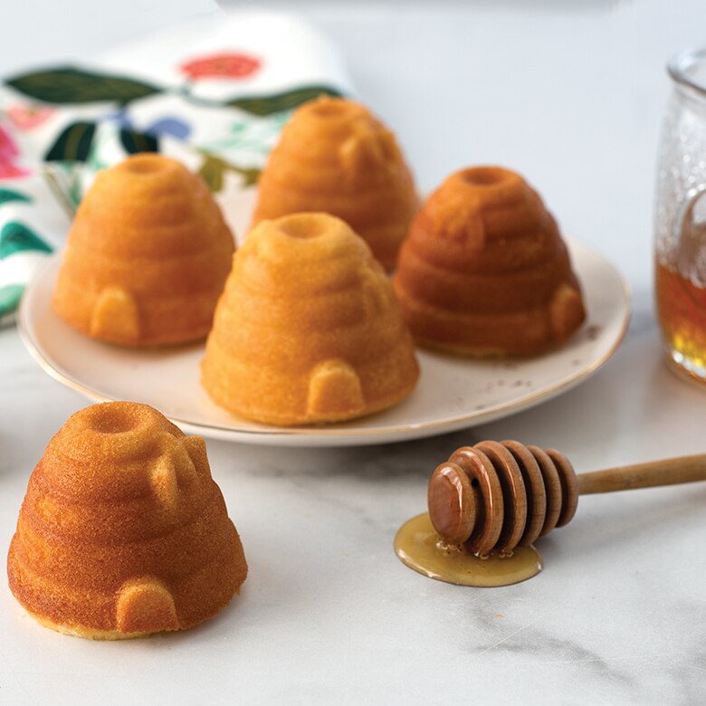 Small honeycomb-shaped cakes on a plate with a honey dipper and jar of honey.